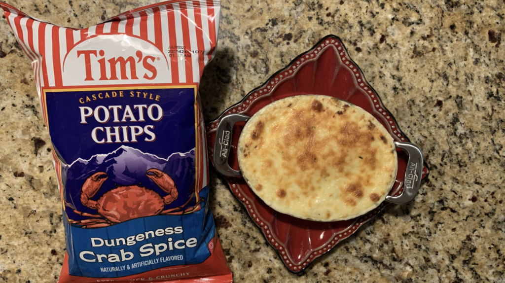 A bag of potato chips next to a pan of cheesy crab dip.